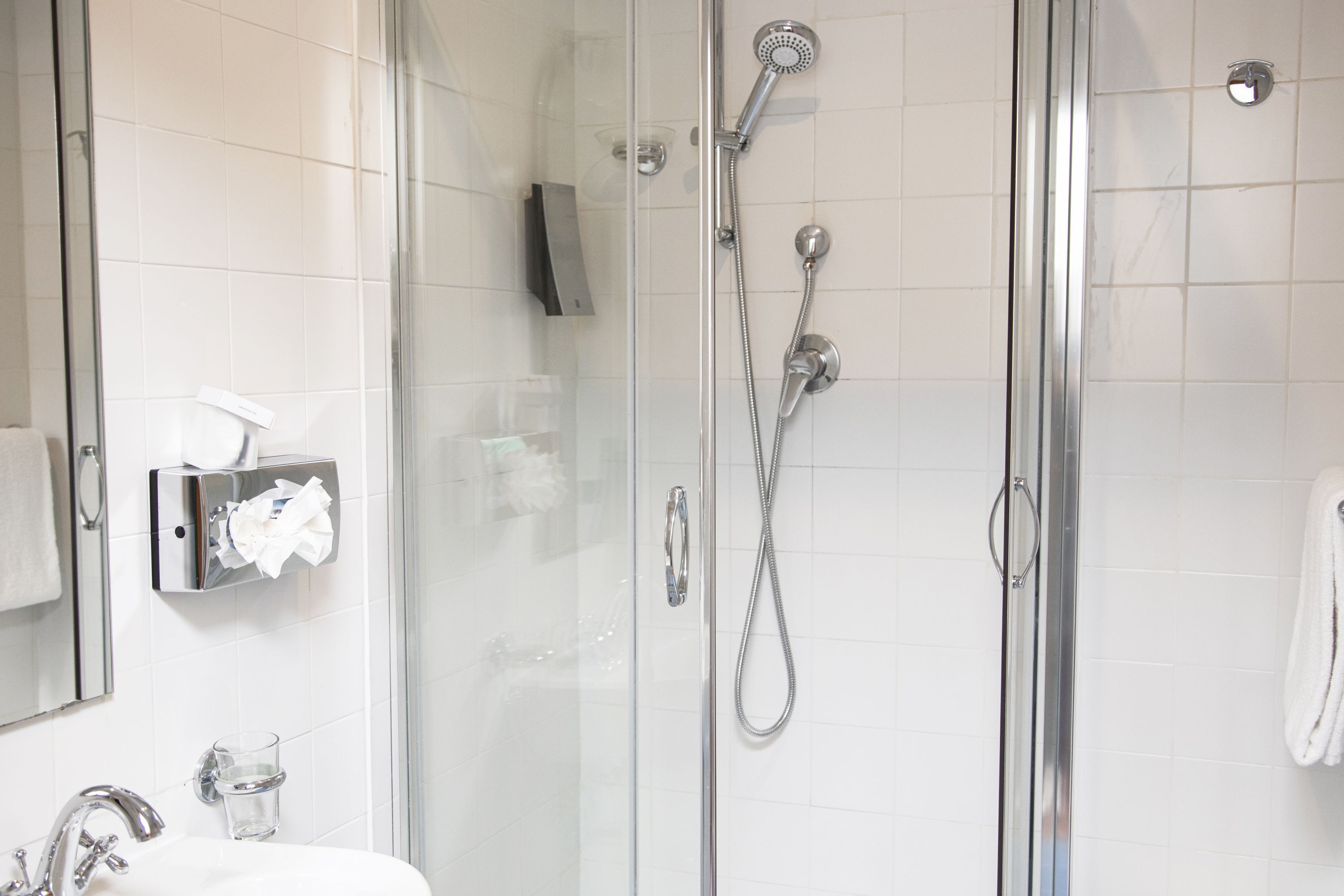A modern bathroom with a glass-enclosed shower, a white sink, and a towel rack.