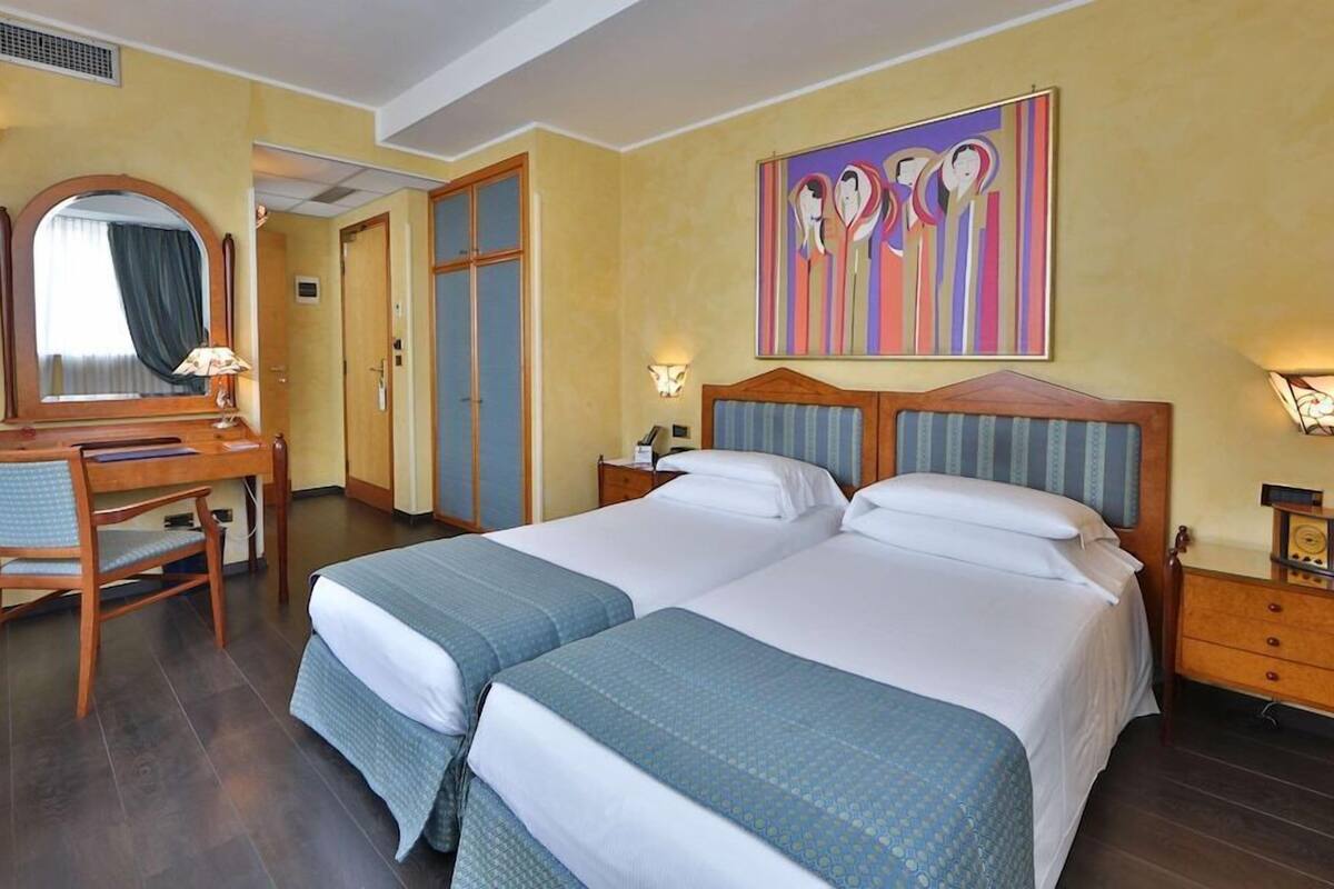 Une chambre d’hôtel avec deux lits, un bureau, une chaise, un miroir et un tableau au mur.