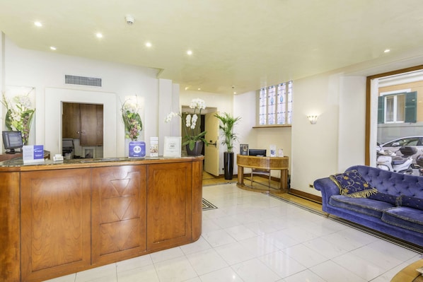 A reception area with a wooden counter, a blue sofa, and potted plants. - Best Western Hotel Artdeco (Rome)