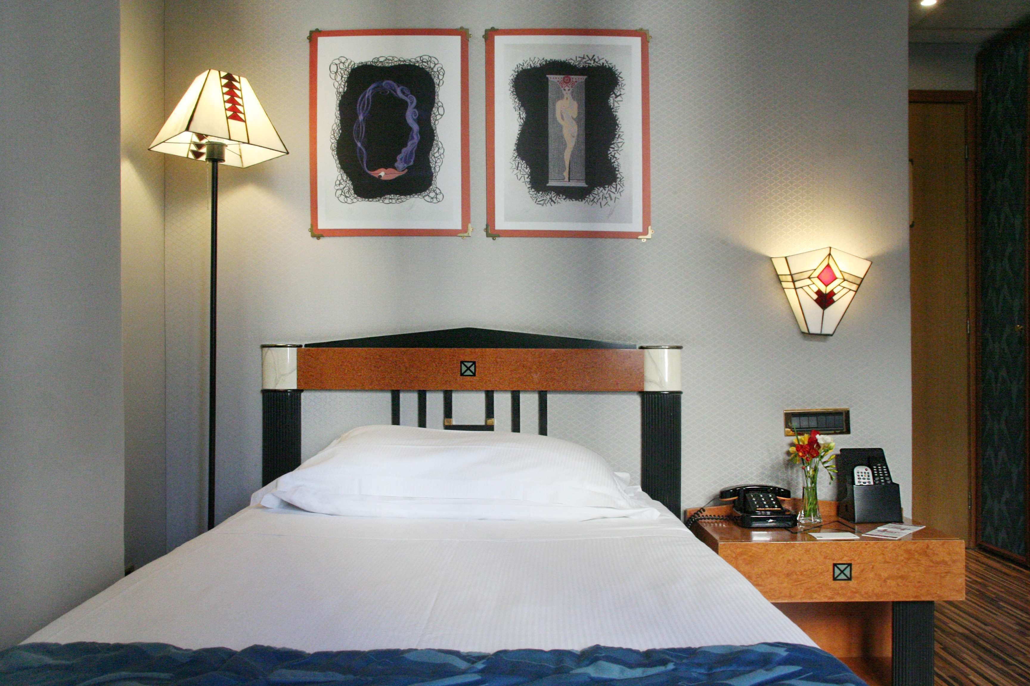 Habitación de hotel con cama, escritorio, teléfono, lámpara y dos cuadros en la pared.