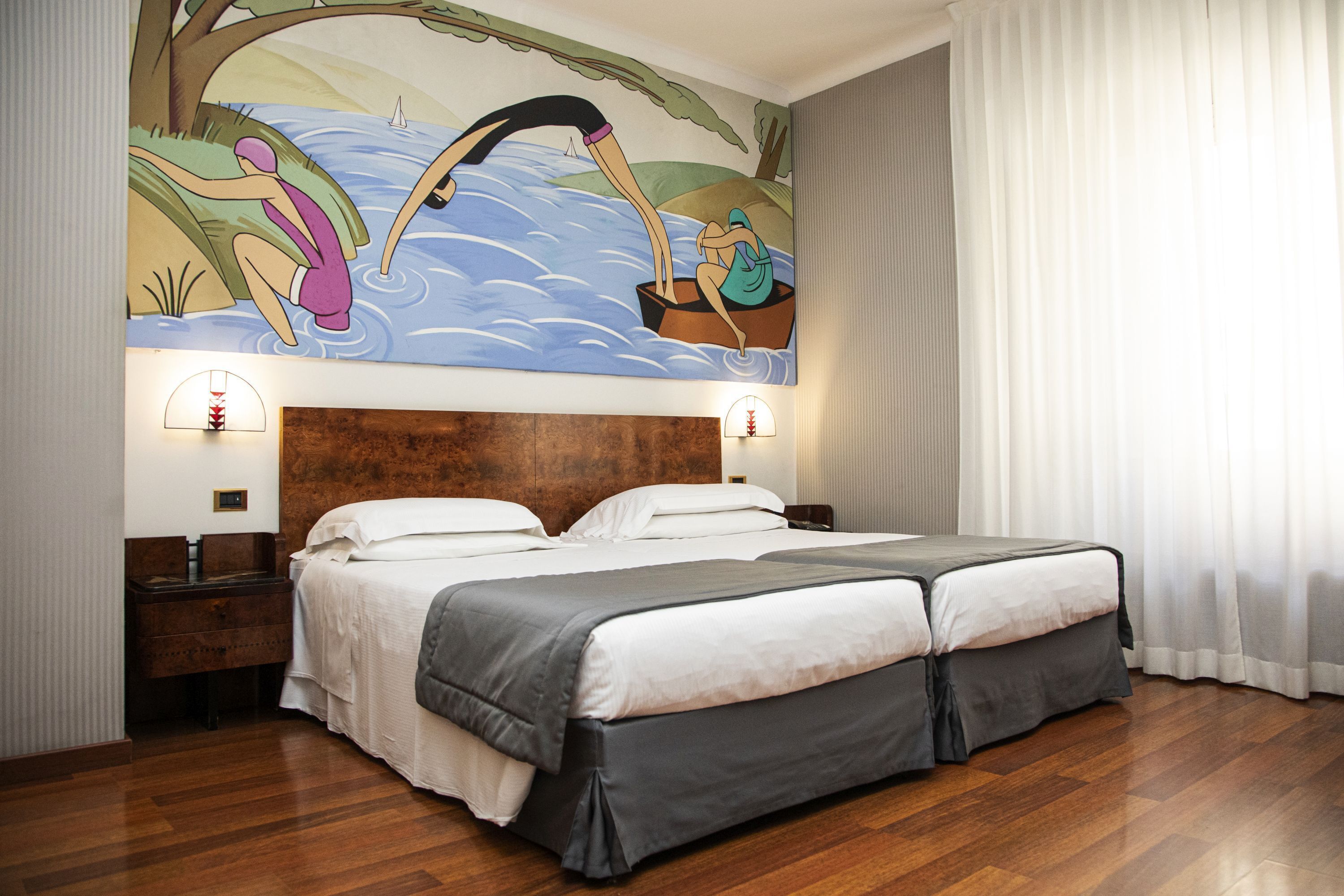 Una cama doble con cabecera de madera, dos mesitas de noche con lámparas y un mural con escena de pesca en la pared.