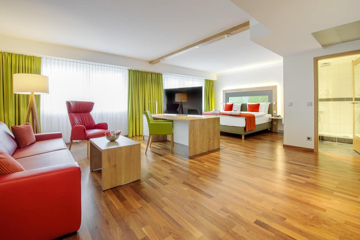 A modern hotel room with a red sofa, a desk, and a bed with orange pillows.