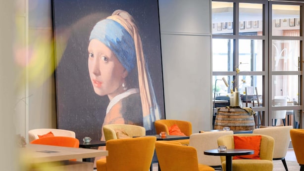 A modern interior with a large painting, orange chairs, and a wooden barrel.