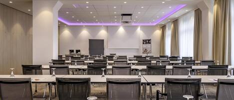 Un salón de conferencias con mesas, sillas y una pantalla para proyector.