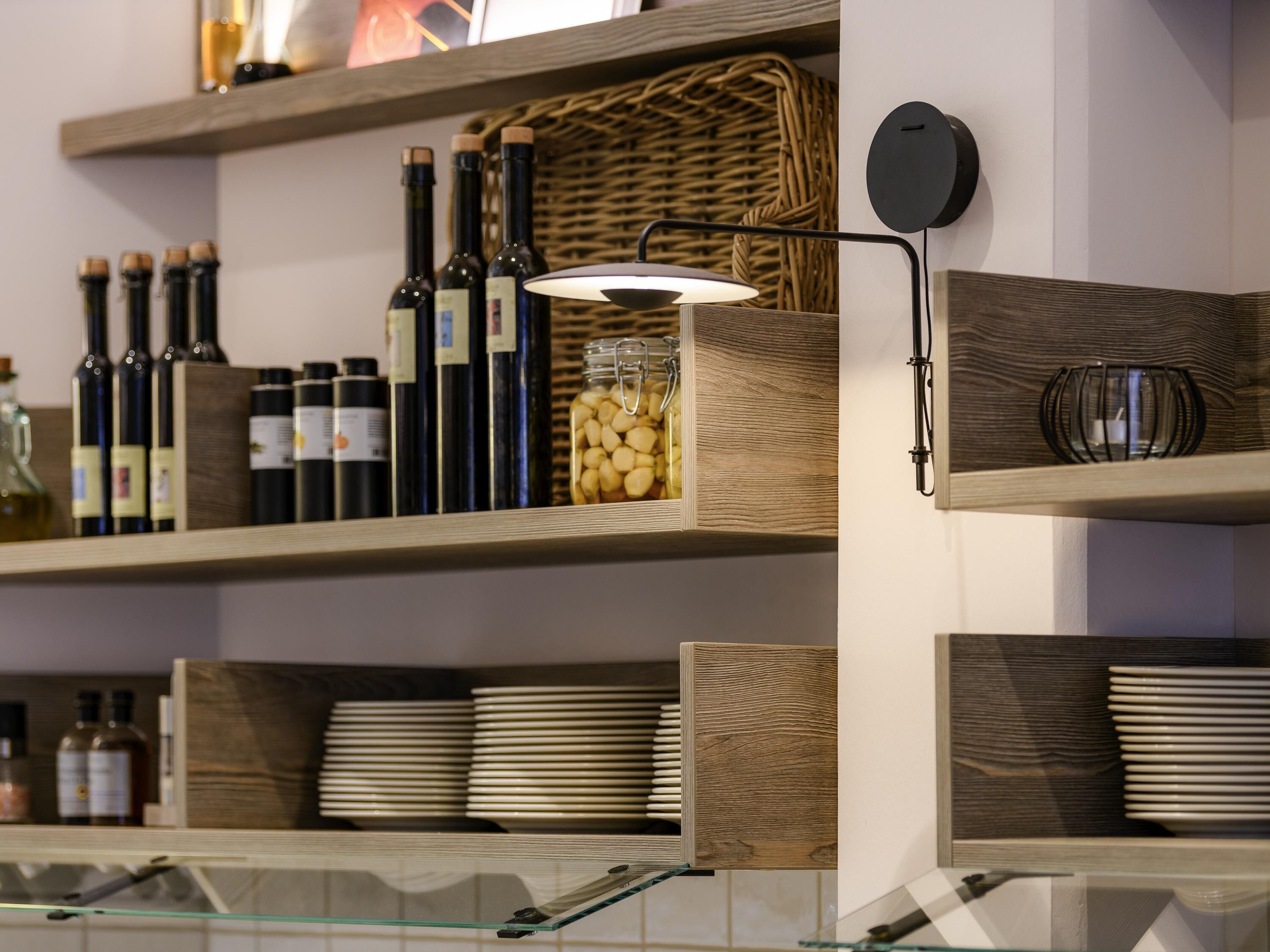 A kitchen with wooden shelves holding wine bottles, a jar of nuts, and stacked plates.