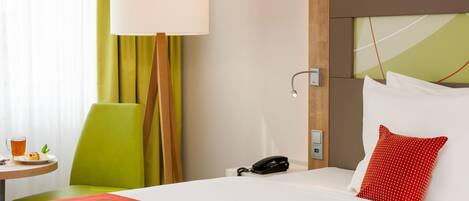 Una habitación de hotel con cama, mesita de noche, lámpara, silla y teléfono.
