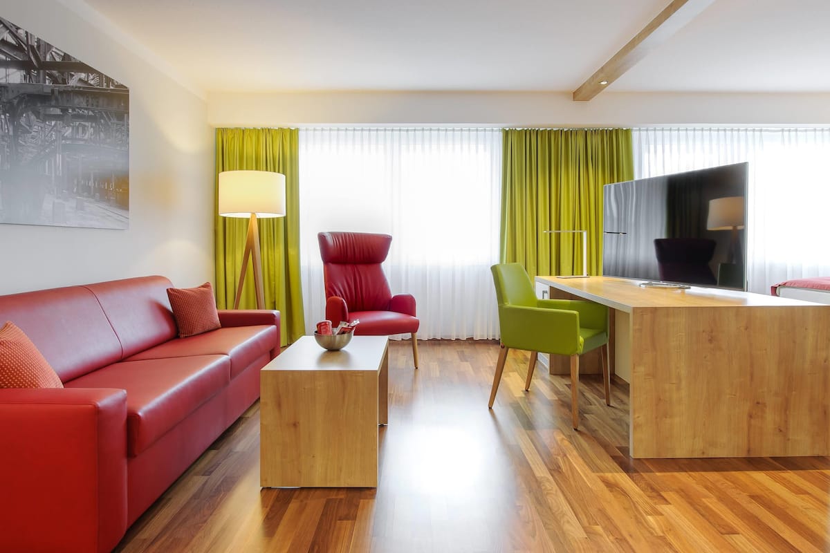 Un salon moderne avec un canapé rouge, un fauteuil vert, une table basse en bois et un téléviseur.