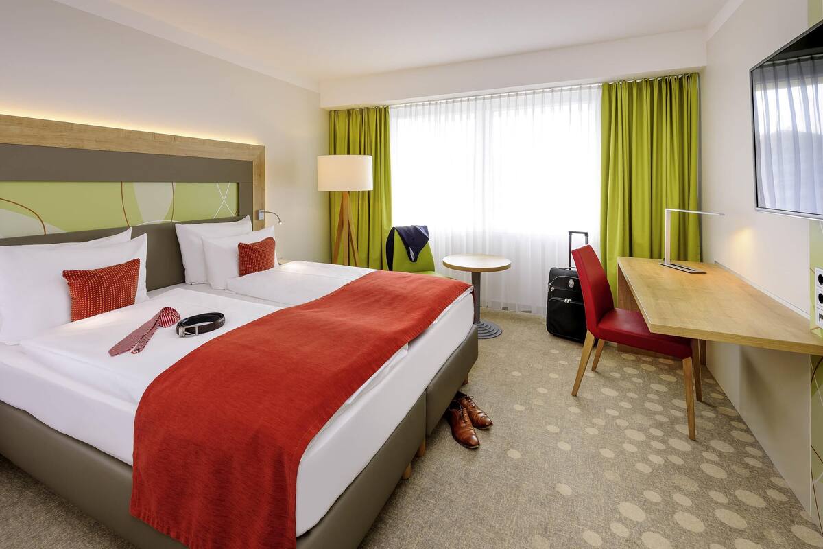 Une chambre d’hôtel avec un lit, un bureau, une chaise, une valise et un téléviseur.