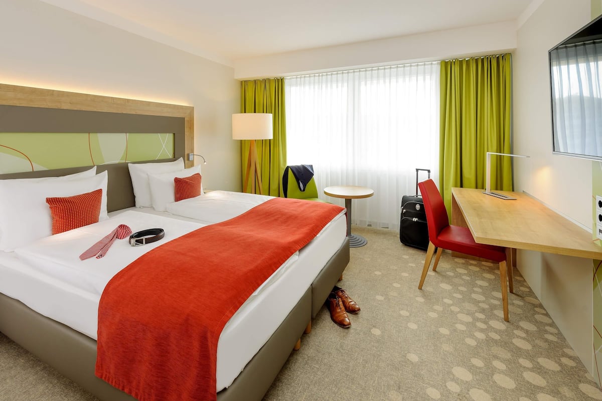 A hotel room with a bed, a desk, a chair, a suitcase, and a television.