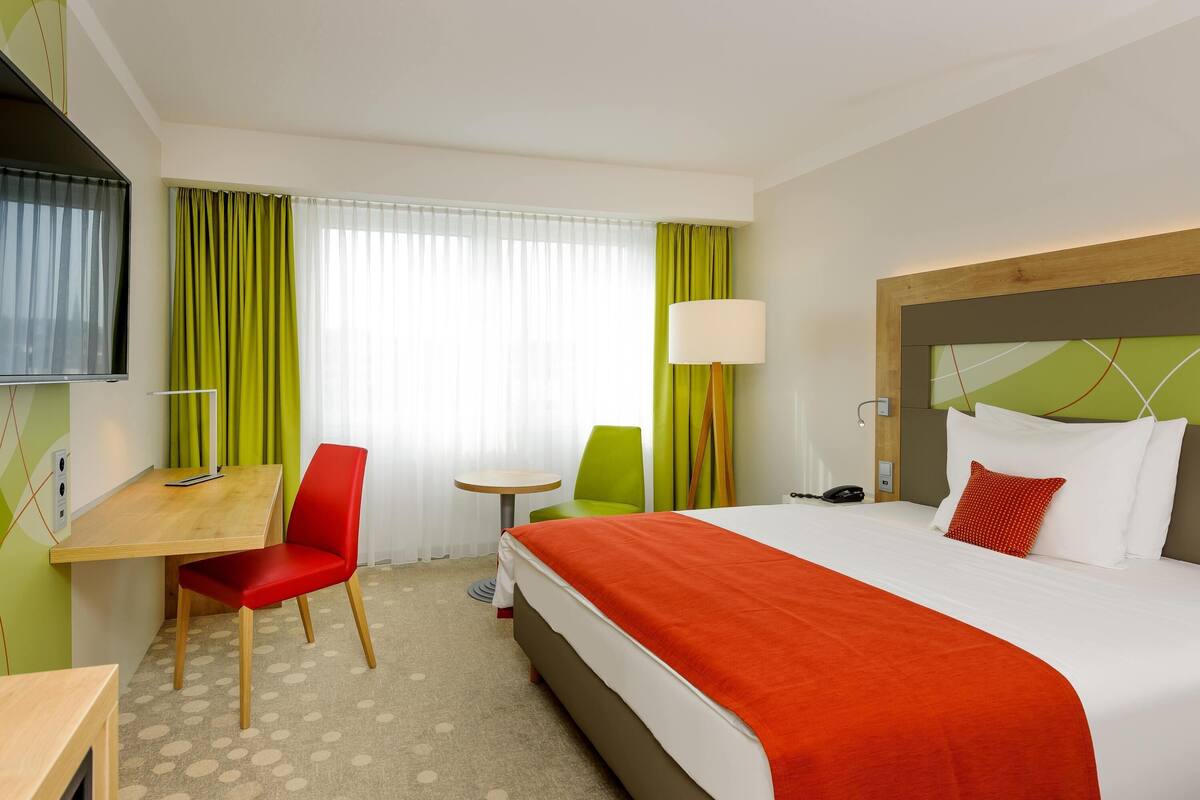 Une chambre d’hôtel équipée d’un lit, d’un bureau, d’une chaise, d’une lampe et d’un téléviseur.