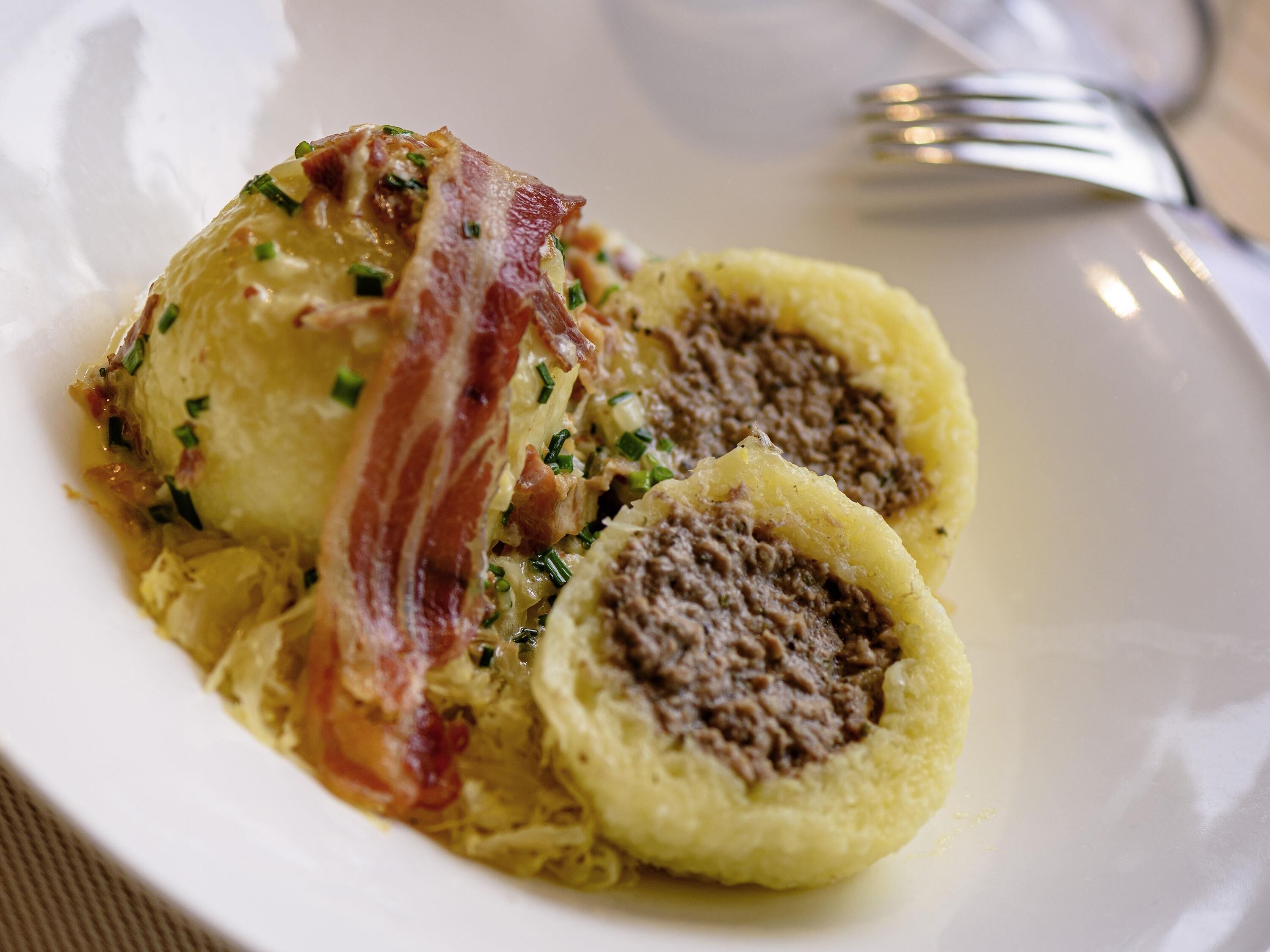 A plate with dumplings, a piece of bacon, and a fork on a table.