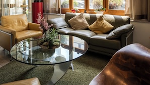 A modern living room with a glass coffee table, leather sofas, and a large window with curtains. - GAIA Hotel Basel - the sustainable hotel (Basel)