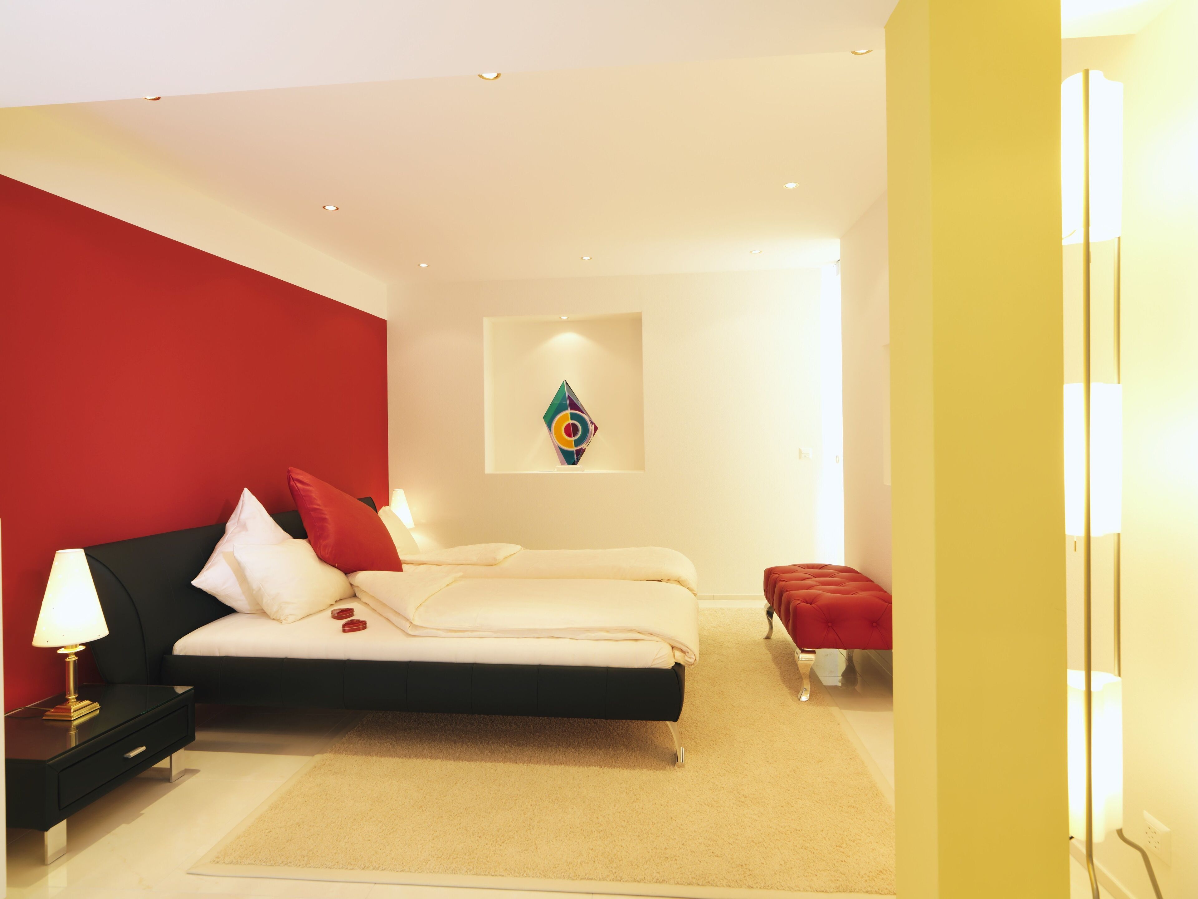A modern bedroom with a bed, nightstand, and a red accent wall.