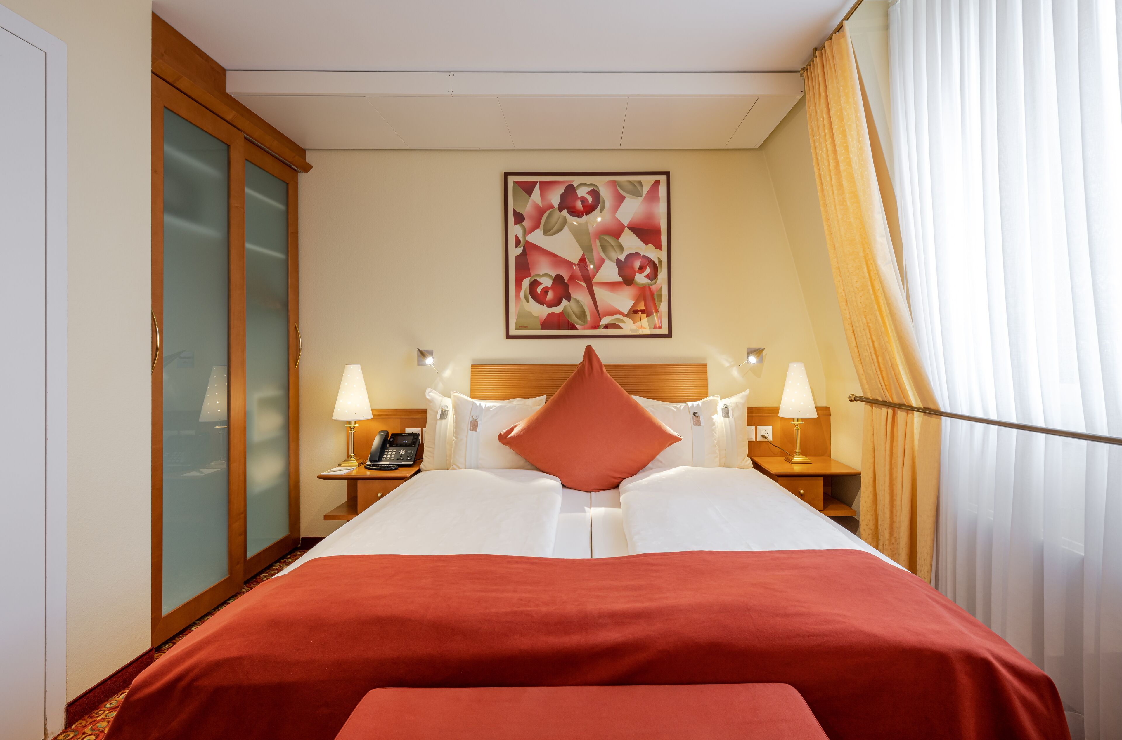 A hotel room with a bed, two bedside tables, a telephone, and a painting on the wall.