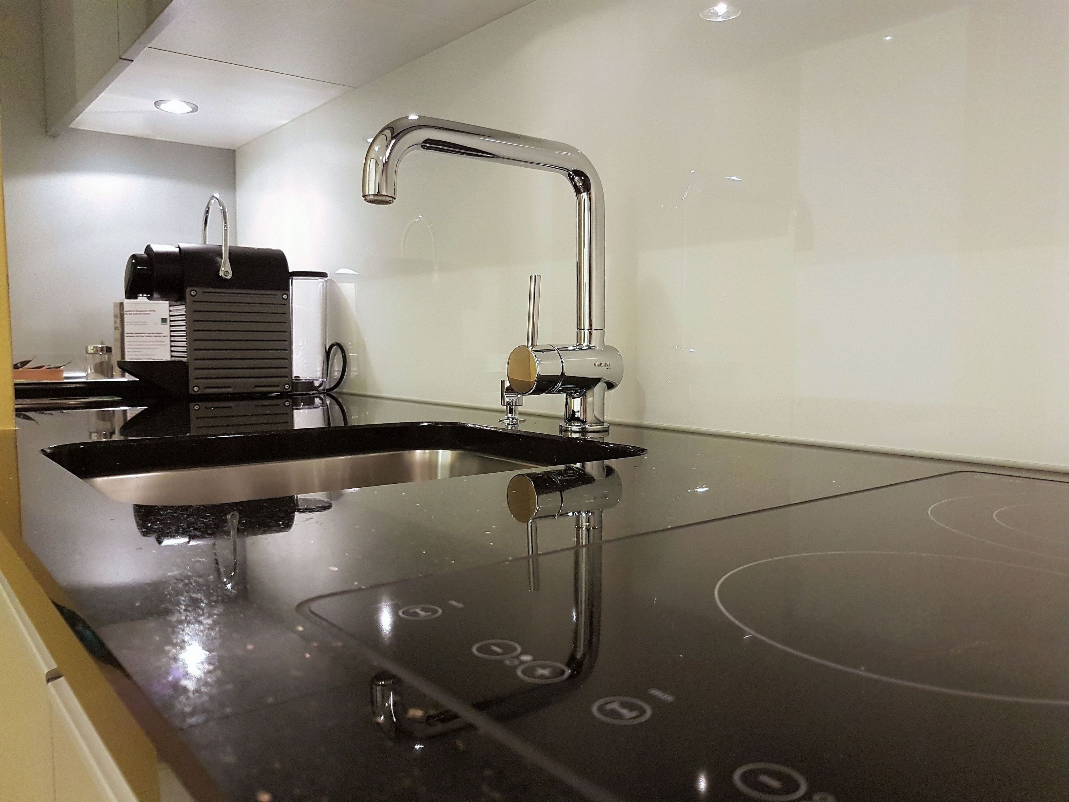 A modern kitchen with a stainless steel sink, a built-in oven, and a coffee machine.