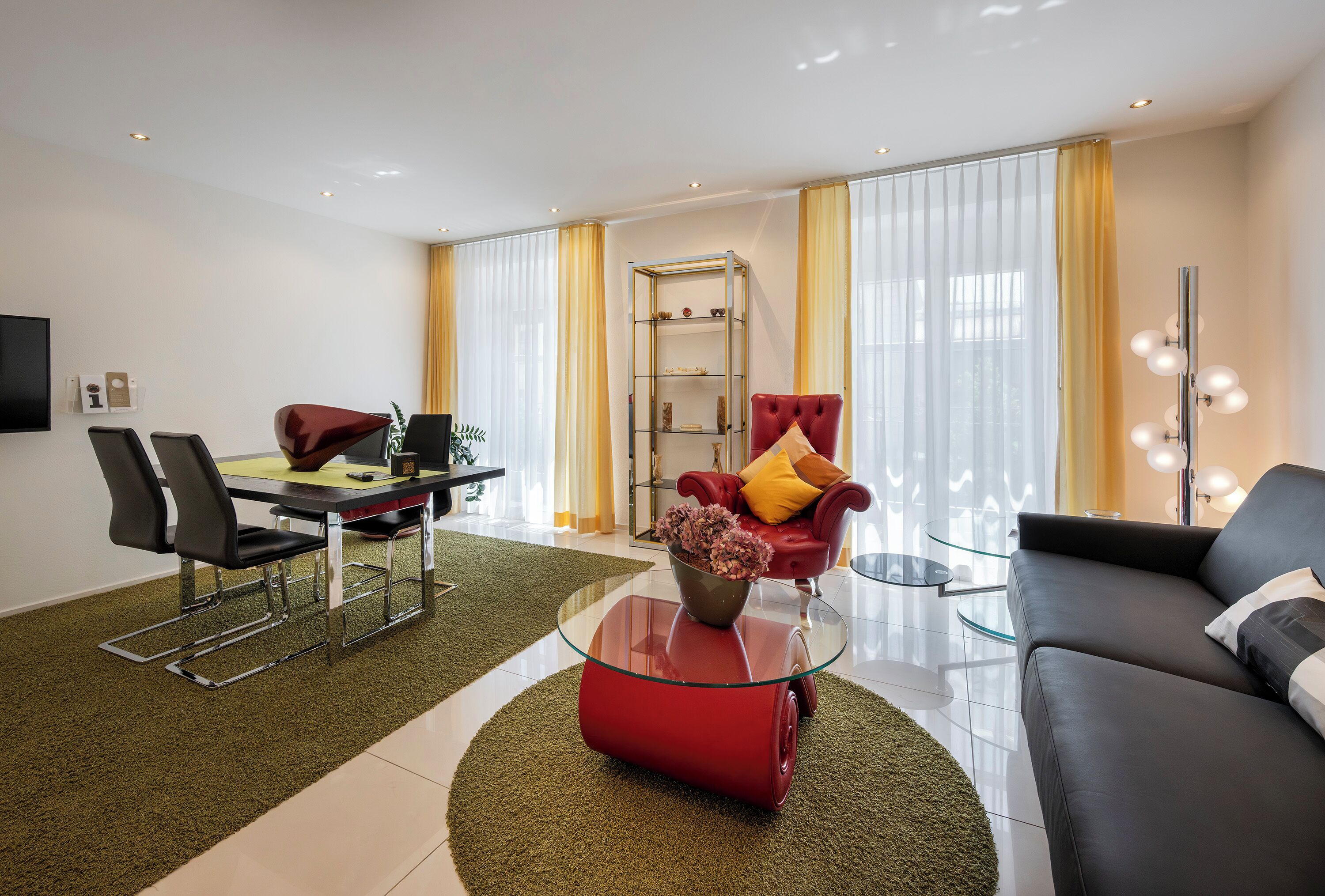 A modern living room with a dining area, a red sofa, a glass coffee table, and a TV mounted on the wall.