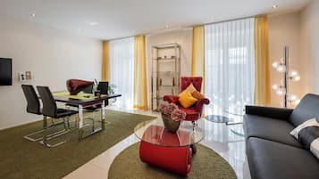 A modern living room with a dining area, a red sofa, a glass coffee table, and a TV mounted on the wall.