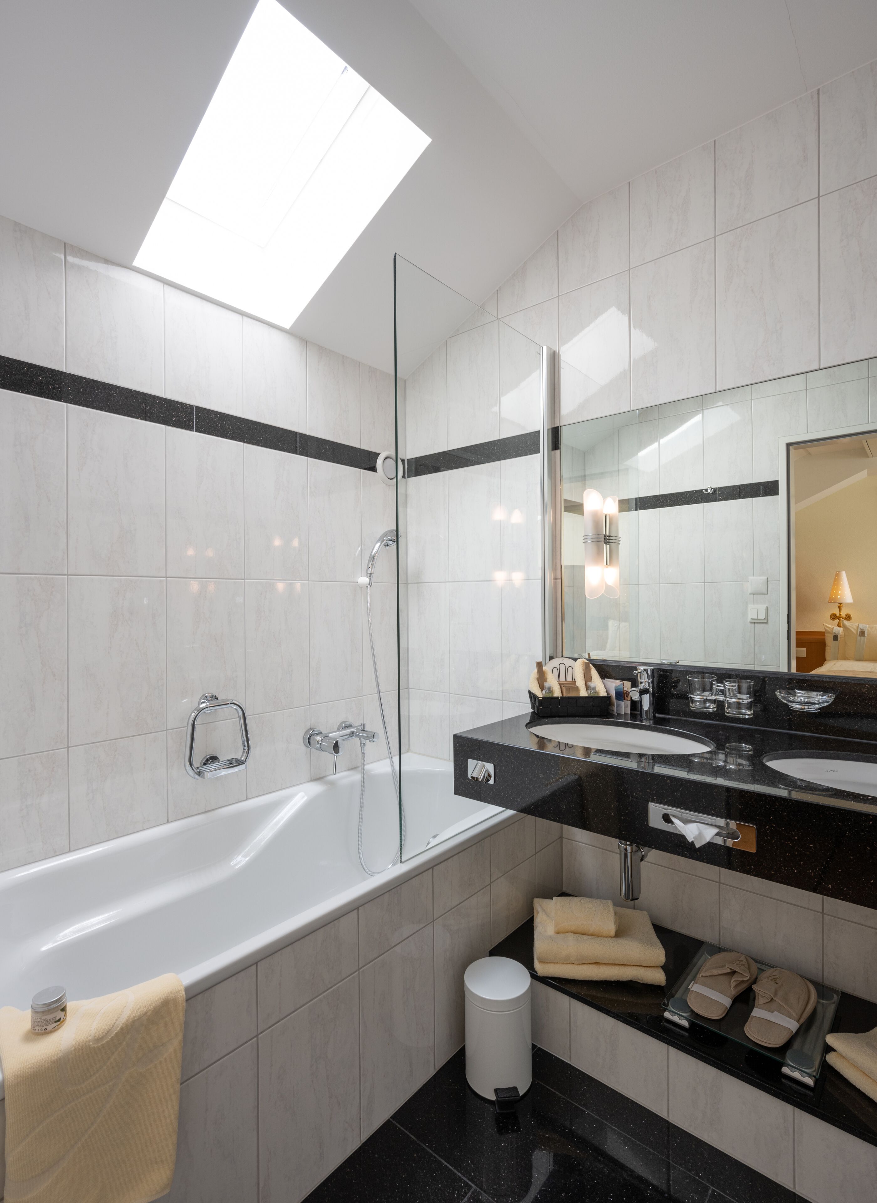 A modern bathroom with a large bathtub, a glass-enclosed shower, and a black countertop with a sink and mirror.
