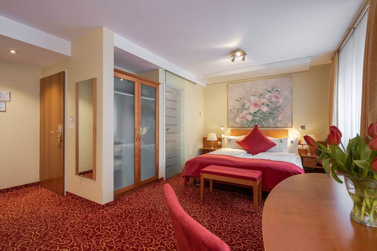 A hotel room with a bed, bedside table, lamp, and a painting on the wall.