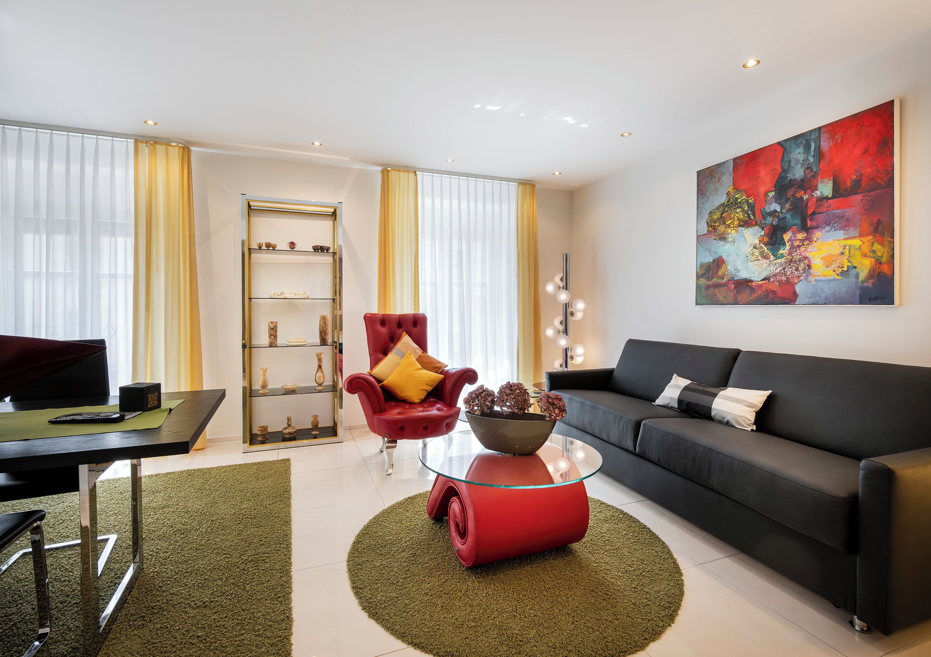 Un salon moderne avec un fauteuil rouge, un canapé noir, une table basse en verre et un bol décoratif.