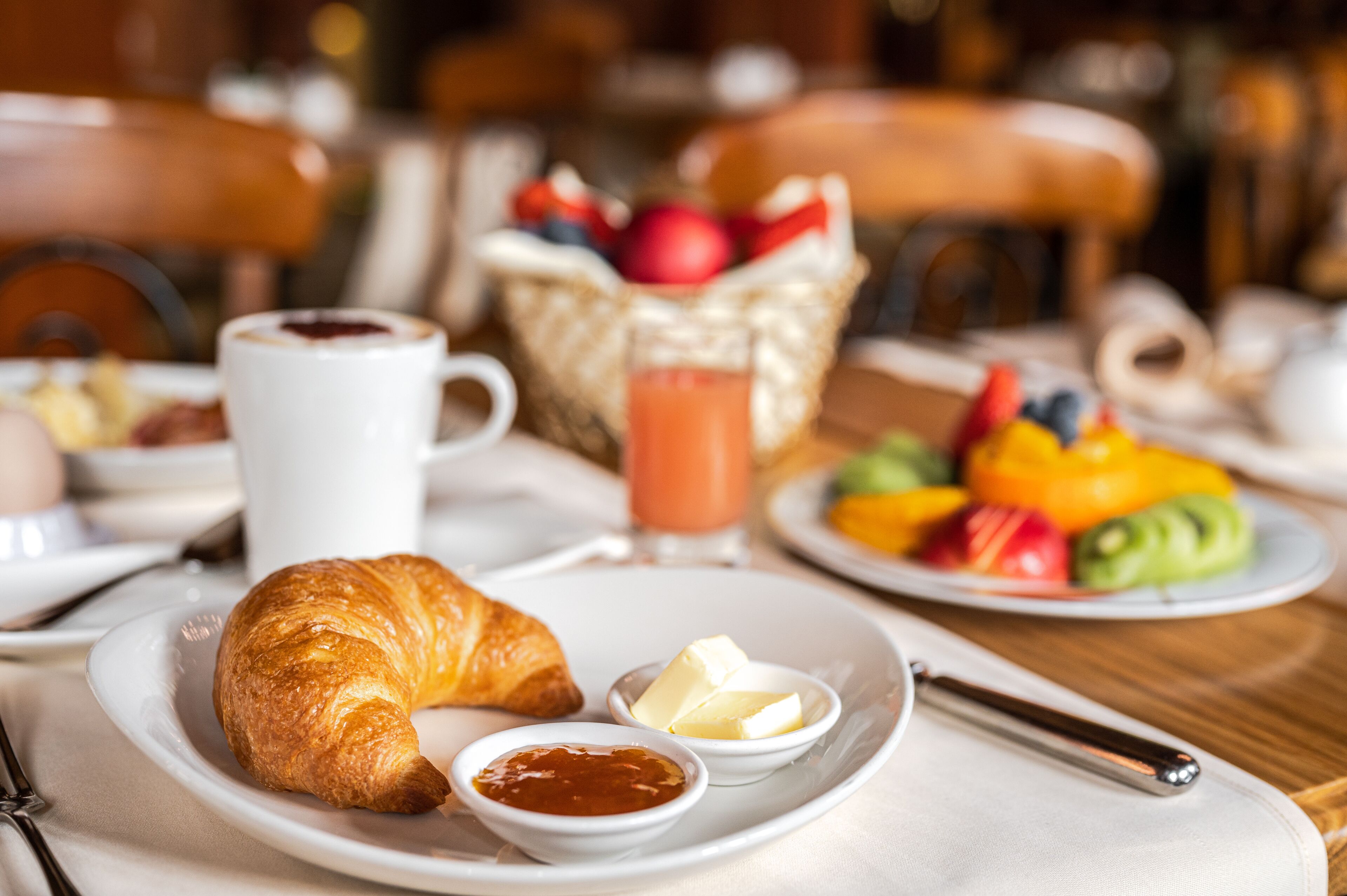 Un desayuno con cruasanes, mantequilla, mermelada y un bol de fruta.
