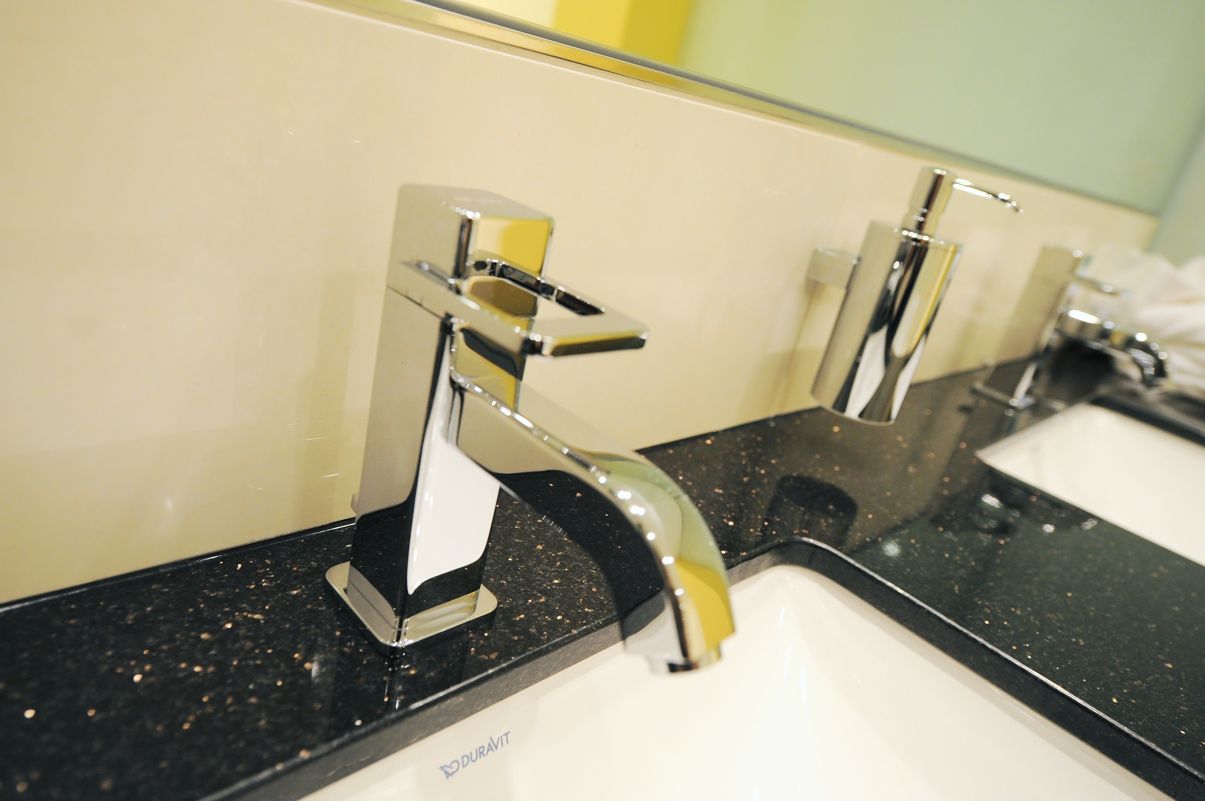 A bathroom with two chrome faucets on a black countertop and a mirror above them.