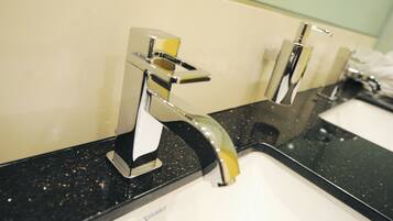 A bathroom with two chrome faucets on a black countertop and a mirror above them.
