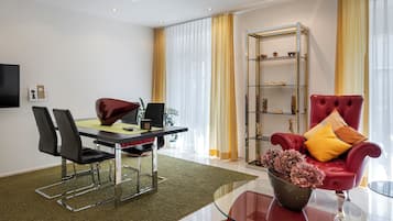 Una sala moderna con una mesa de centro de vidrio, un sillón de cuero rojo, un área de comedor con mesa y sillas, y una estantería.