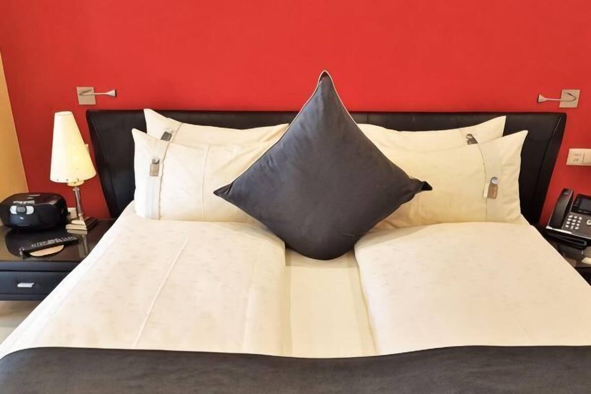 A bed with a black headboard, white and grey pillows, a black telephone, and a lamp on a bedside table.