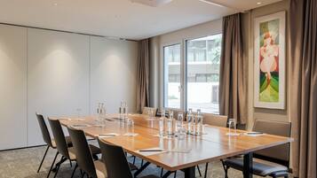 Ein Konferenzraum mit einem langen Tisch, Stühlen, einem Projektor und einem Fenster mit Vorhängen.