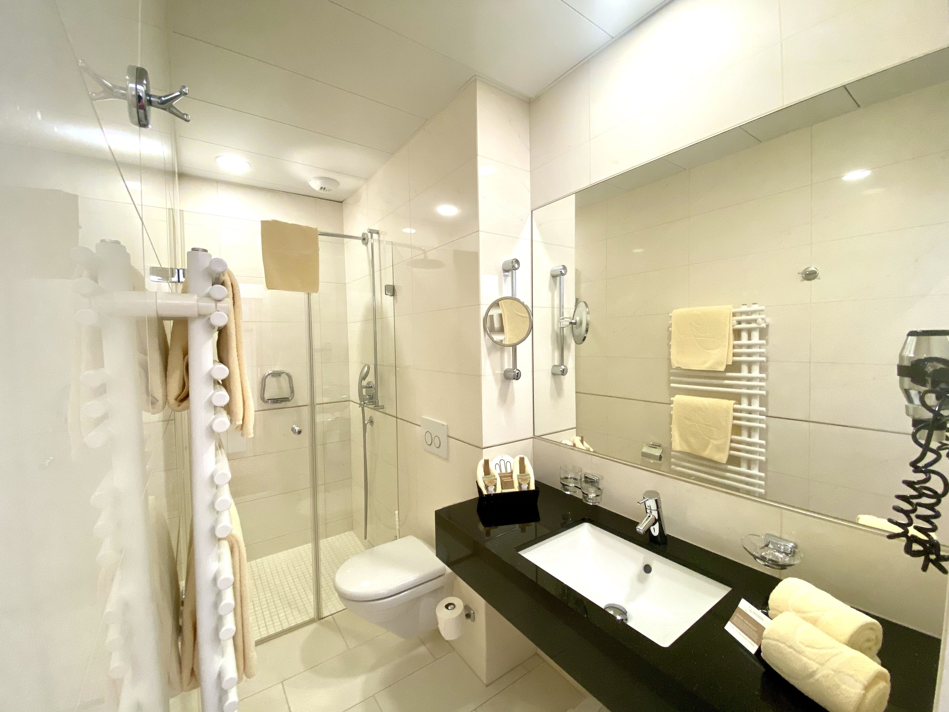 A modern bathroom with a glass-enclosed shower, a white toilet, a black sink with a mirror, and towels on the counter.