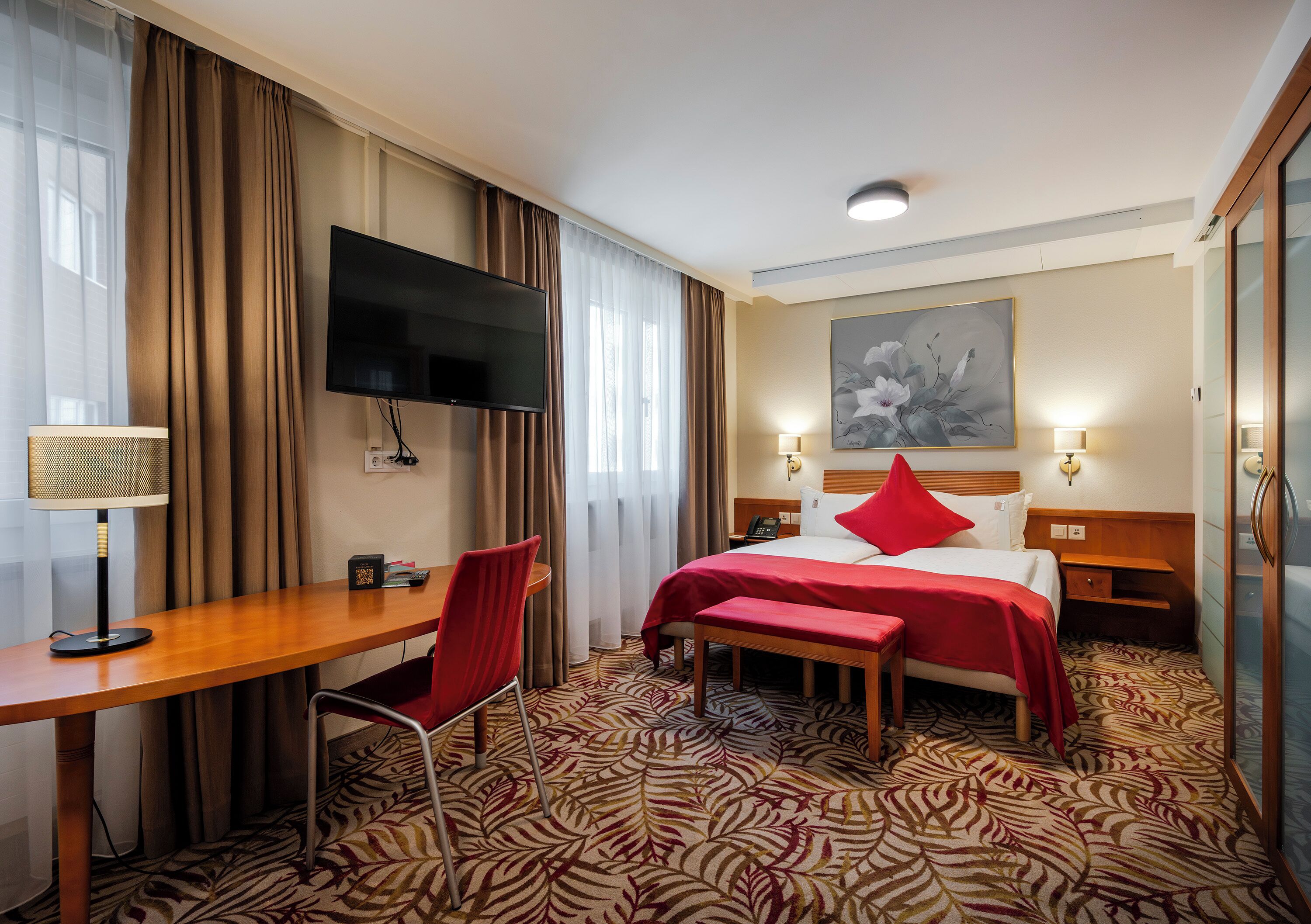 A hotel room with a bed, desk, chair, television, and artwork on the wall.
