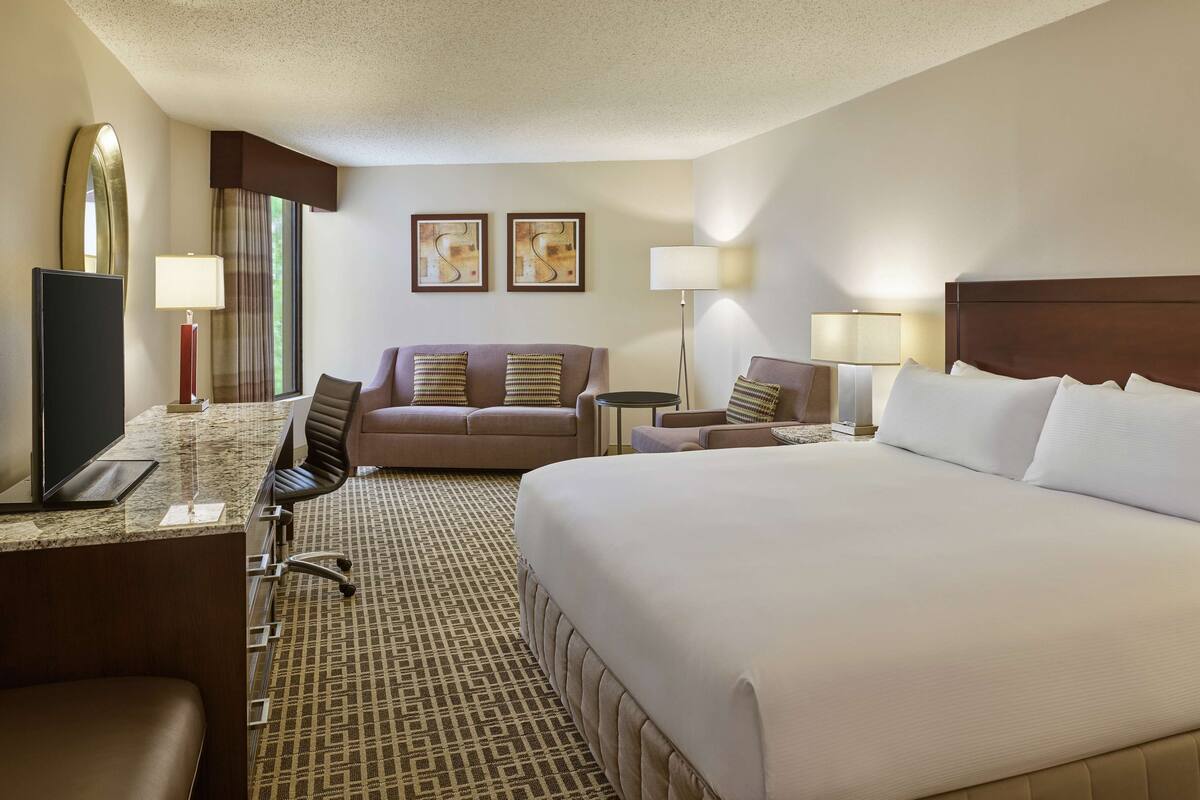 Ein Hotelzimmer mit einem großen Bett, einem Schreibtisch mit Computer, einer Couch, zwei Sesseln und einem kleinen Tisch.