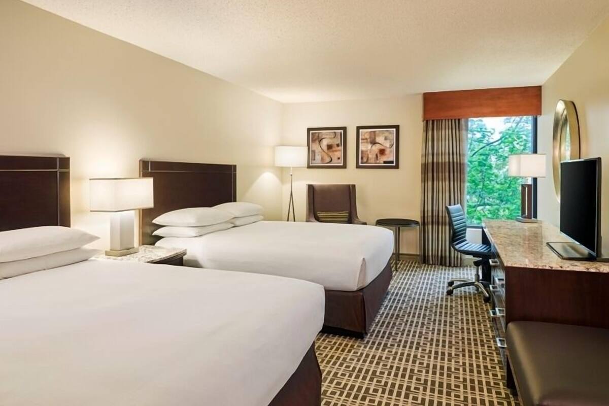 Ein Hotelzimmer mit zwei Betten, einem Schreibtisch, einem Computer, einem Stuhl und einem Fernseher.