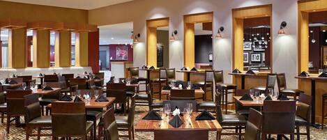 Un restaurante amplio con varias mesas y sillas, detalles de madera y cuadros en las paredes.