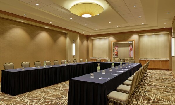 Un salón de conferencias con una mesa larga, sillas y una alfombra estampada.