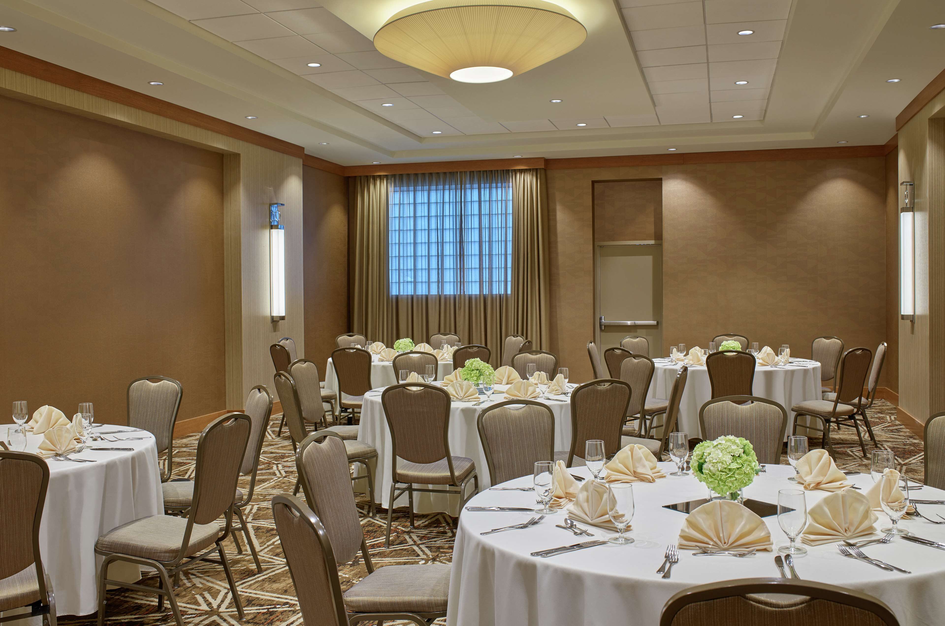A banquet hall with round tables set for dining, arranged in rows, and equipped with chairs.