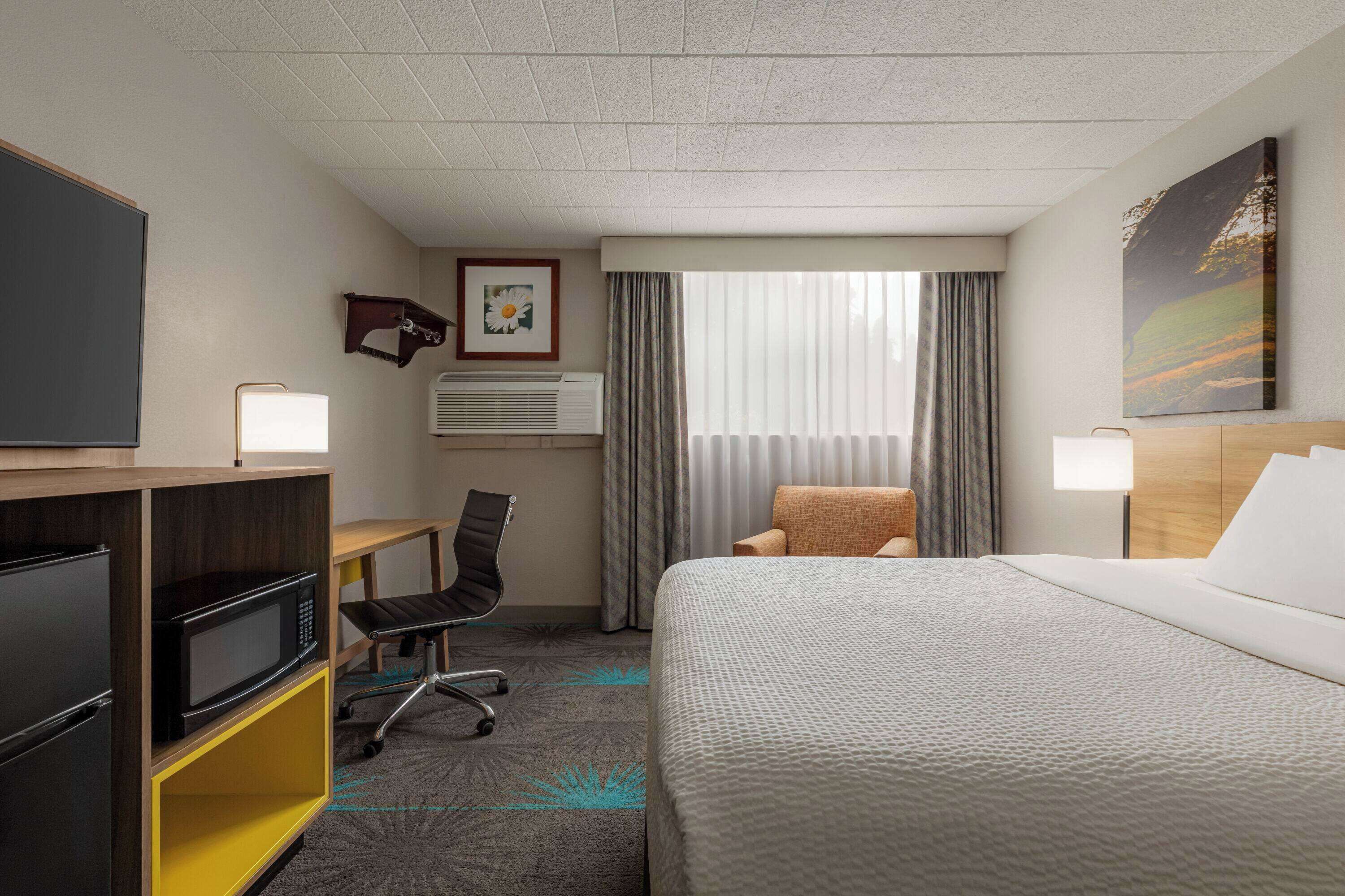 Une chambre d’hôtel équipée d’un lit, d’un bureau, d’une chaise, d’une télévision et d’une fenêtre avec des rideaux.