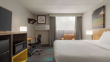 Une chambre d’hôtel équipée d’un lit, d’un bureau, d’une chaise, d’une télévision et d’une fenêtre avec des rideaux.