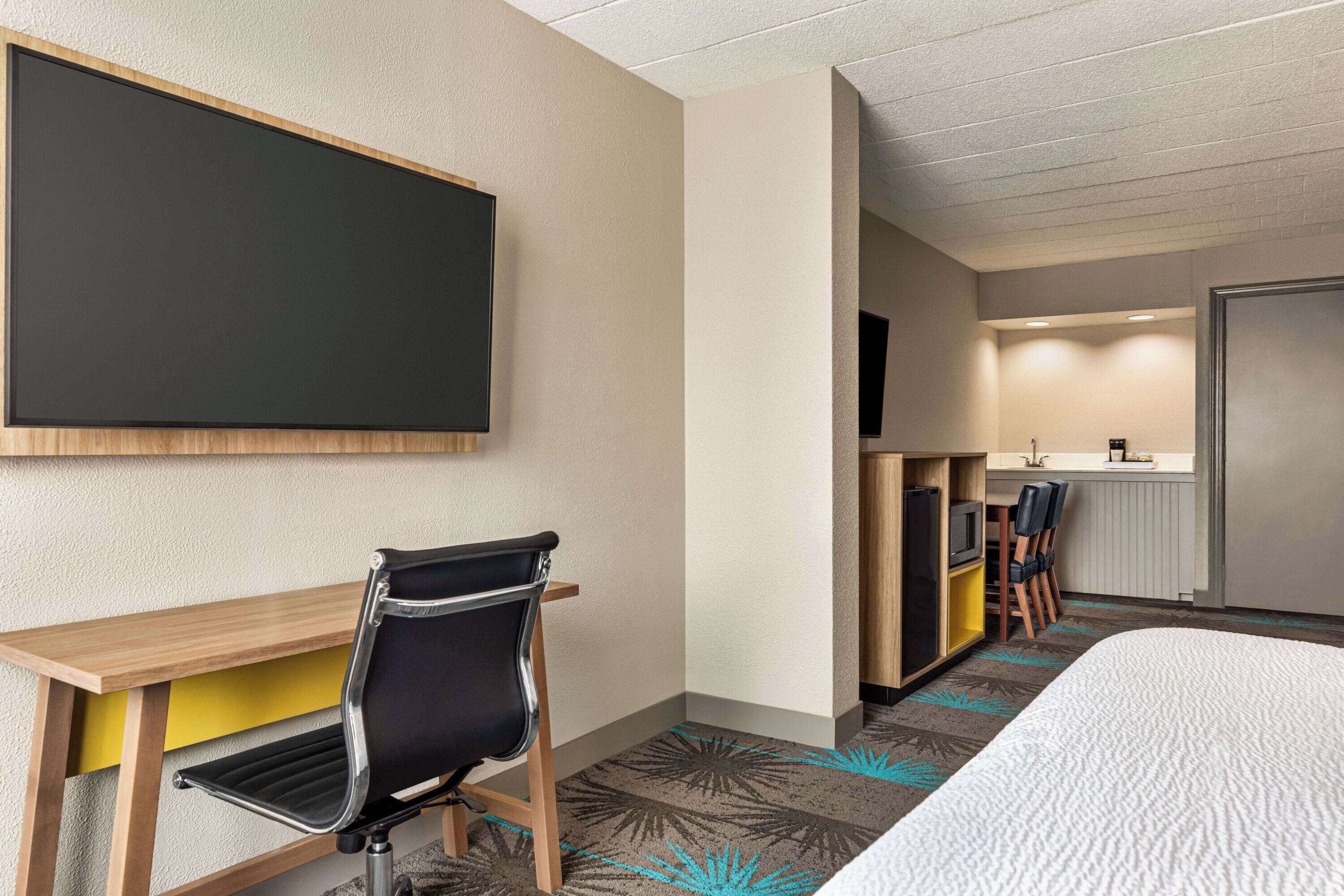 Une chambre d’hôtel équipée d’un lit, d’un bureau, d’une chaise, d’une télévision et d’une kitchenette.