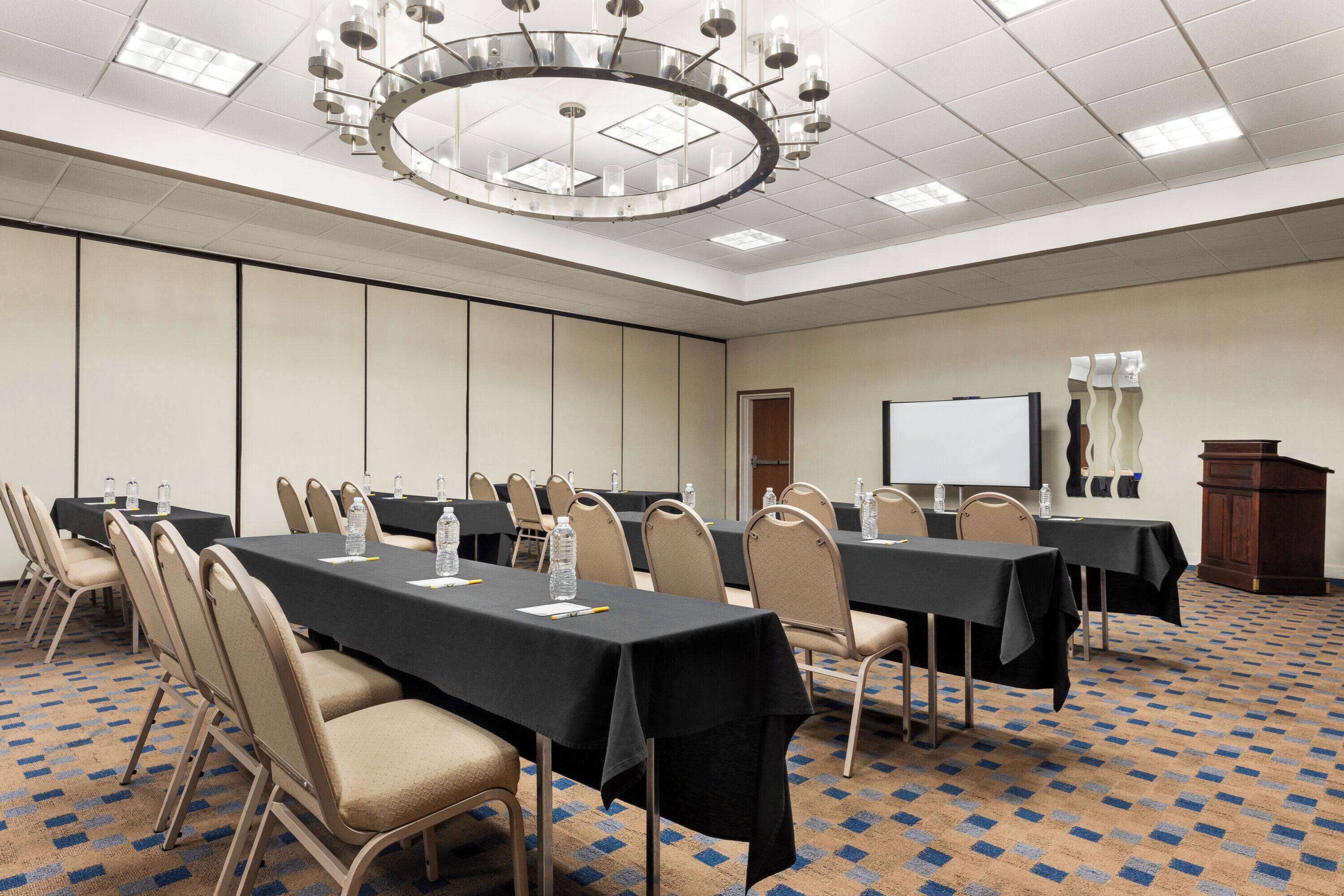 A conference room with multiple tables, chairs, a projector screen, and a podium.