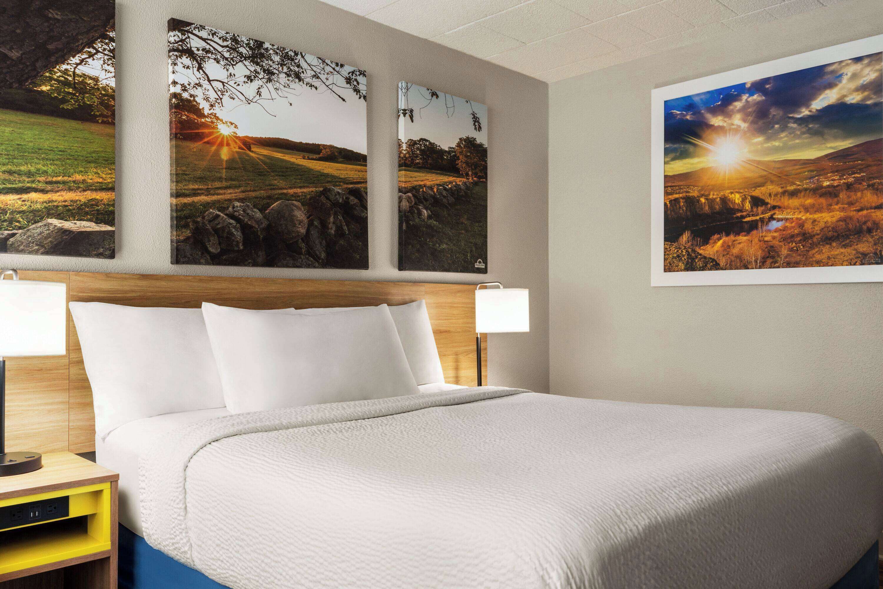 A hotel room with a large bed, two bedside tables, and three framed landscape paintings on the wall.