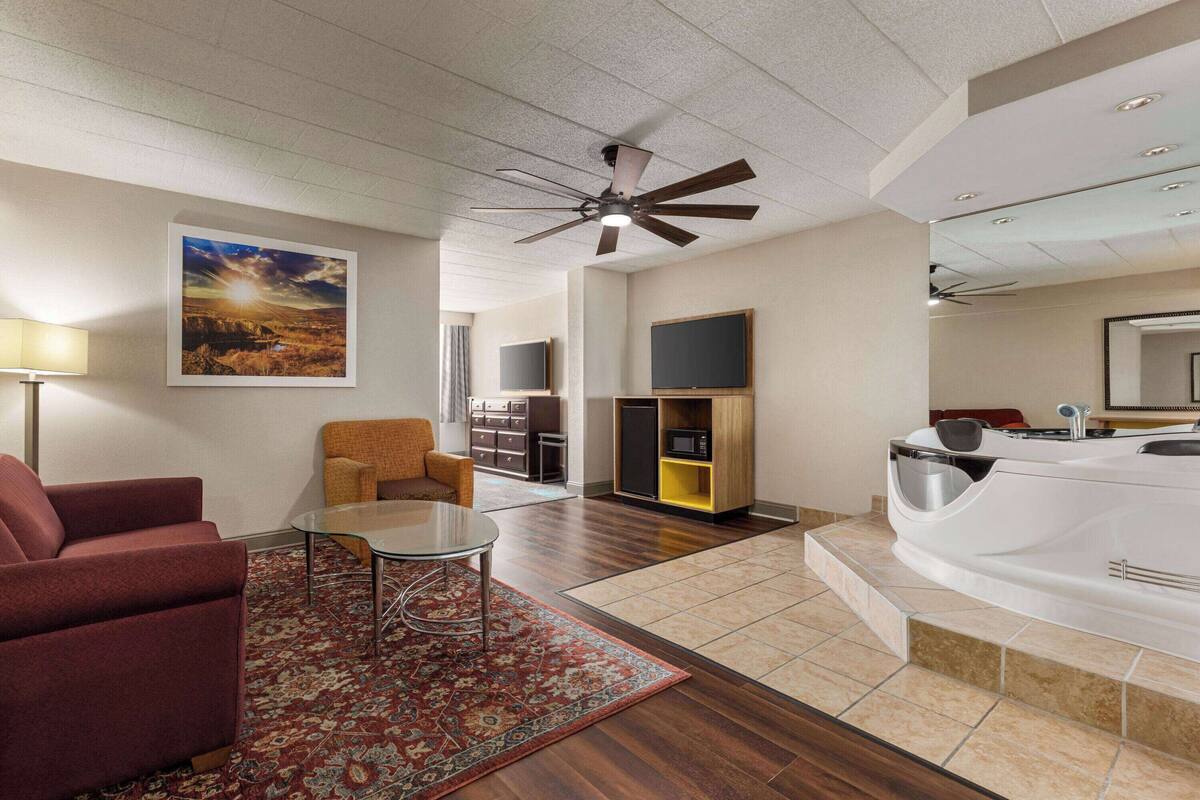 Ein modernes Wohnzimmer mit einem roten Sofa, einem Glastisch, einem gemusterten Teppich, einem Deckenventilator, einem Flachbildfernseher, einem Holzkabinett und einer Whirlwanne.