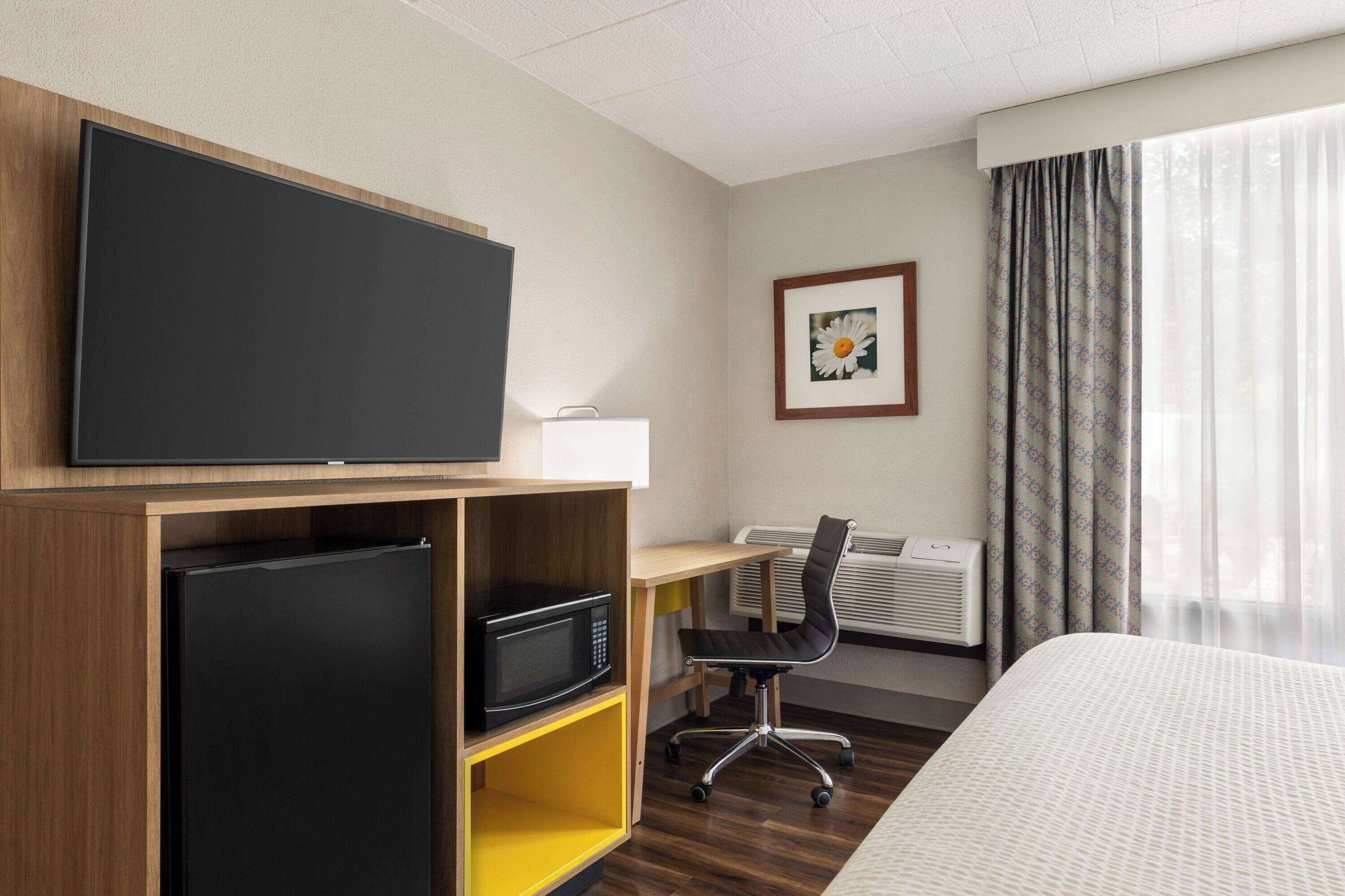 A hotel room with a bed, a desk with a chair, a flat-screen TV, a microwave, and a small refrigerator.