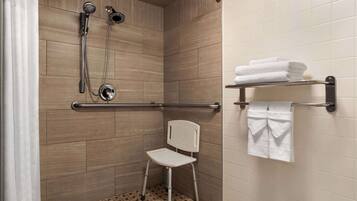 A shower area with a grab bar, a chair, and a towel rack with folded towels.