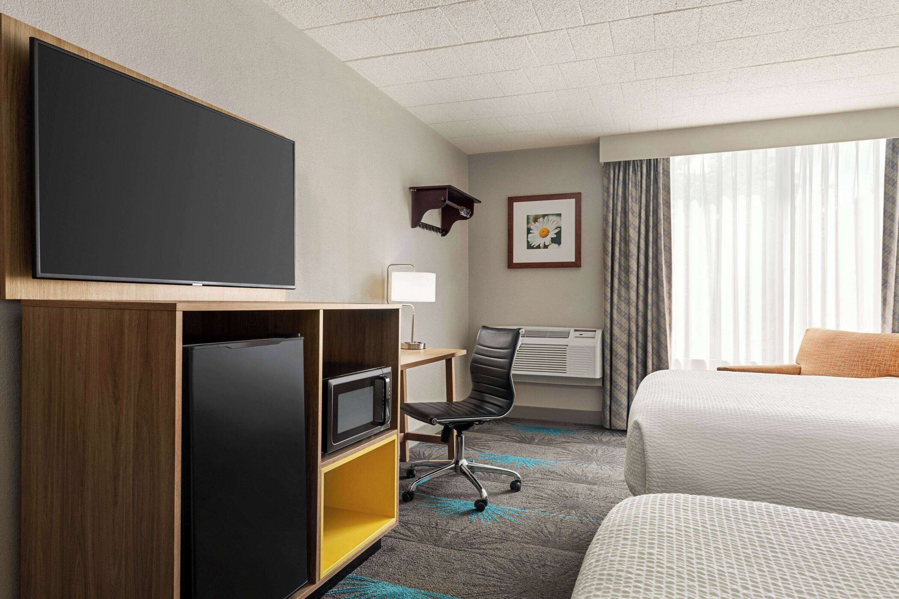 A hotel room with a bed, a desk with a computer, a flat-screen TV, a microwave, and a chair.