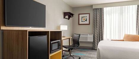 A hotel room with a bed, a desk with a computer, a flat-screen TV, a microwave, and a chair.