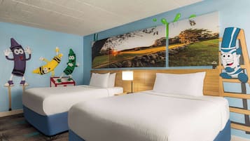 Two beds with white mattresses and blue headboards, a large wall mural, and a small table with a lamp.