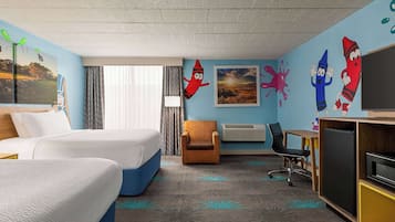A hotel room with two beds, a desk, a chair, a TV, and colorful wall decorations.