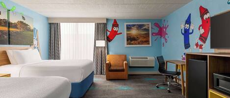 A hotel room with two beds, a desk, a chair, a TV, and colorful wall decorations.